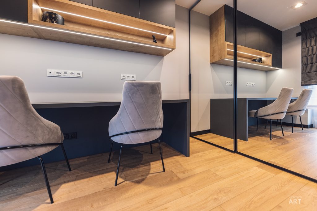 Nowoczesne biuro z dwoma stanowiskami pracy wyposażonymi w białe krzesła tapicerowane, drewniane półki z oświetleniem LED oraz czarno-białe biurka. Wnętrze utrzymane jest w kolorystyce drewna, bieli i czerni, z drewnianą podłogą i lustrzaną ścianą po prawej stronie.