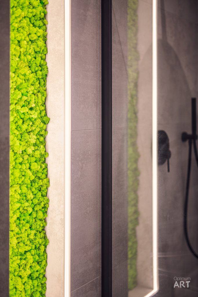 Nowoczesne wnętrze z pionowymi pasami jaskrawozielonego mchu naturalnego wkomponowanymi w jasne ściany. W tle widoczna łazienka z prysznicem i minimalistycznym designem.
