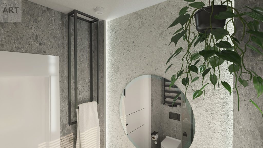 Nowoczesna łazienka z betonowymi ścianami, w której widać okrągłe lustro odbijające toaletę, czarną ramę z ręcznikami oraz zieloną roślinę zwisającą z sufitu.