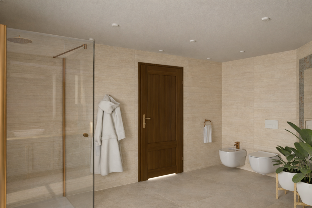 Nowoczesna łazienka w jasnych, beżowych tonach z kabiną prysznicową ze szklaną ścianką, dwoma białymi miskami WC oraz bidetem. Na ścianie wisi biały szlafrok, a w rogu stoi roślina doniczkowa na złotym stojaku.