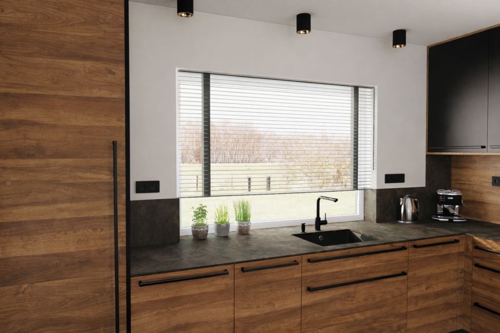 Nowoczesna kuchnia z drewnianymi szafkami, czarnym blatem i zlewem pod oknem z żaluzjami. Na blacie stoją doniczki z roślinami oraz sprzęty kuchenne, a nad wyspą wiszą czarne lampy sufitowe.