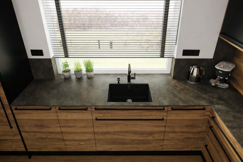 Nowoczesna kuchnia z drewnianymi szafkami, ciemnym blatem i czarnym zlewozmywakiem pod oknem z żaluzjami. Na parapecie stoją trzy doniczki z ziołami, a na blacie widać czajnik elektryczny i ekspres do kawy.