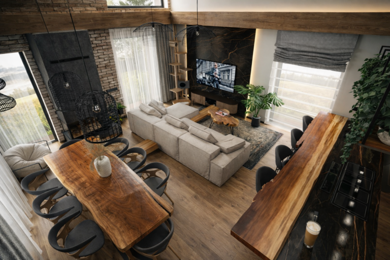 Nowoczesny salon z otwartą przestrzenią, w którym znajduje się szara sofa, drewniany stół jadalny z czarnymi krzesłami oraz wyspa kuchenna. Wnętrze charakteryzuje się industrialnym stylem z ceglanymi ścianami, drewnianymi belkami sufitowymi i dużymi oknami.