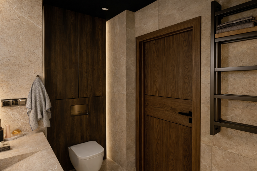 Nowoczesna łazienka z beżowymi kafelkami na ścianach, drewnianymi elementami wykończeniowymi i białą miską ustępową. Po prawej stronie widoczny jest czarny grzejnik ścienny, a centralne miejsce zajmują drewniane drzwi z ciemnym wykończeniem.